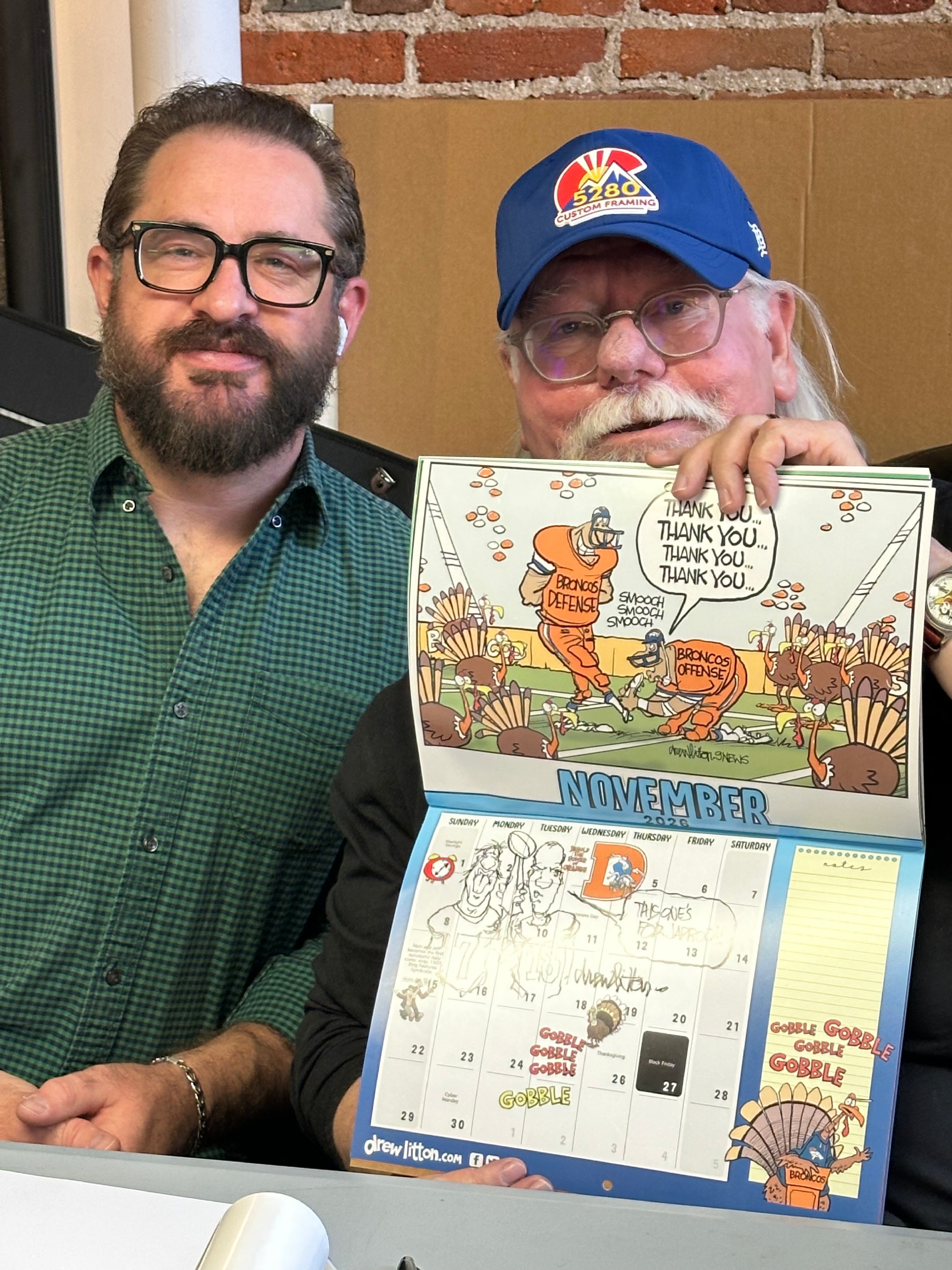 Denver sports cartoonist Drew Litton with his custom framed signed Broncos calendar at 5280 Custom Framing